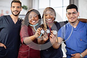 Four young multiethnic medical practitioners, standing together in hospital room with stethoscopes