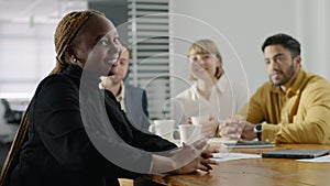 Four young multiracial adults in businesswear smiling and talking in meeting room in office