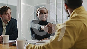 Four young multiracial business people in businesswear shaking hands in meeting at office