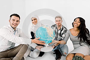 Four young multiracial people holding hands and hug Earth globe, sitting on the floor, on the white background. Save the