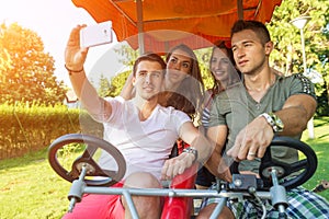 Four young people in a four-wheeled bicycle, they do selfie photo
