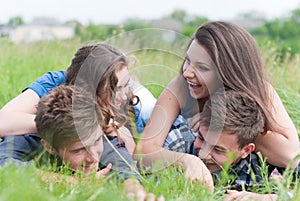 Four young people friends lying together on green grass outdoors