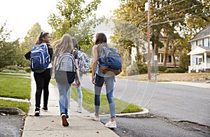 Four young teen girls walking to school together, back view