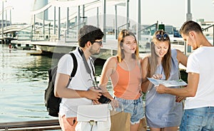 Four young travelers holding map in hands