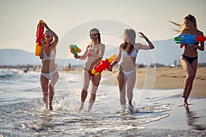 Four young woman at beach playing with water guns. Cheerful group of friends having fun on summer vacation together. Holiday,