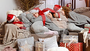 Four young womens in red santa hats fell asleep on the couch after wrapping Christmas presents