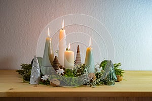 Fourth Advent, decoration with four different lit candles, some moss, green Christmas balls from glass and cinnamon stars on a