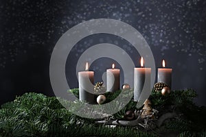 Fourth advent with four burning candles on fir branches with Christmas decoration against a dark grey background, copy space