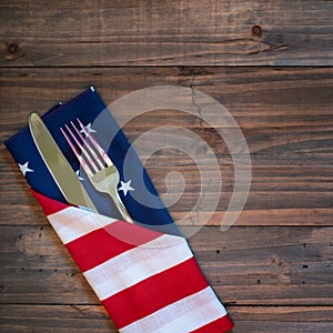 Fourth of July Table Place Setting with a fork, knife and flag napkin on rustic wood board background with room or space for copy,