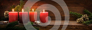 Fourth  Sunday in Advent, four burning red candles in a row, fir branches and Christmas decoration on dark rustic wood, wide