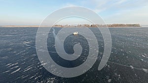 FPV Drone view. Airboat skating on frozen river at sunset near embankment.