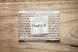 Fragile, handwriting on white squre paper in bubble pack, rought wood background
