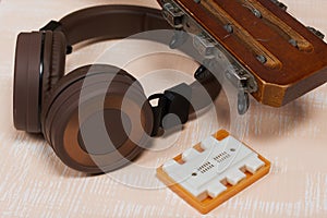 Fragment of acoustic guitar and tuning fork. Nearby are wireless headphones. Against a background painted in white and beige