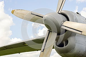 A fragment of airplane wing with four-bladed aircraft propeller against blue sky