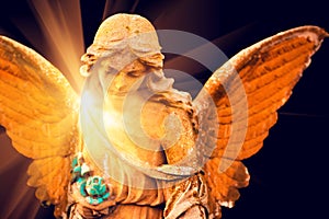 A fragment of ancient sculpture angel in a golden glow in the old cemetery. Symbol of love, invisible forces, purity,