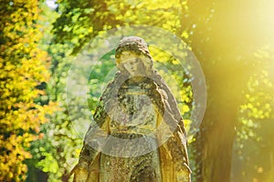 Fragment of an ancient stone statue of Virgin Mary against beautiful landscape of forest in sunlight