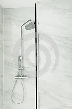 Fragment of bathroom interior with tempered safety glass enclosure with shower fittings head hanging on tiled wall. Modern minimal