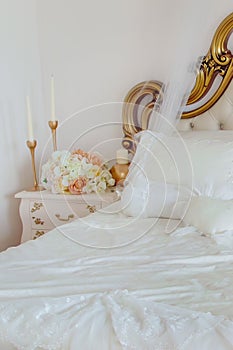 Fragment of bed and bedside table with flowers and candles. Elegant bedroom interior