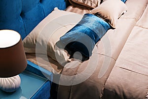Fragment of a bed with a bedside table and a table lamp. Modern bedroom in blue and beige colors. Close-up