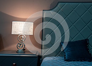 Fragment of a bedroom with a bedside table and a bed. A table lamp is on the nightstand