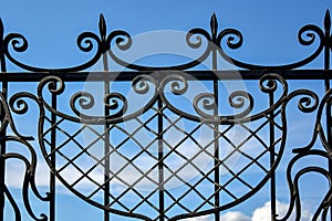 Fragment of black openwork wrought-iron fence grating against blue sky background. Close-up. Copy space.
