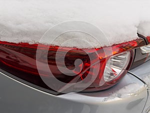 Fragment of car with tail lamps, covered with snow above
