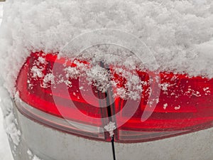 Fragment of car with tail lamps, covered with snow above