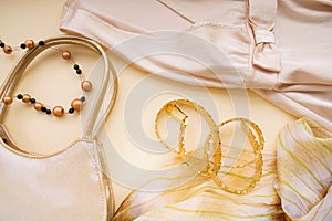 A fragment of a dress and a scarf, handbag, belt and necklace. Top view on a beige background