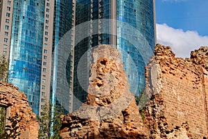 Fragment of the facade of a modern building against the background of the ruins of an old brick building