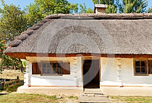 Fragment of the facade of an old traditional Ukrainian rural house with a thatched roof against the backdrop of a summer garden