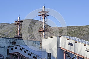 Fragment of factory buildings with pipes against the background of the mountains