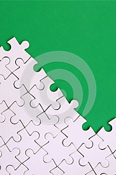 Fragment of a folded white jigsaw puzzle on the background of a green plastic surface. Texture photo with copy space for text.