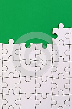 Fragment of a folded white jigsaw puzzle on the background of a green plastic surface. Texture photo with copy space for text