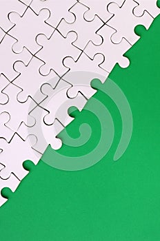 Fragment of a folded white jigsaw puzzle on the background of a green plastic surface. Texture photo with copy space for text