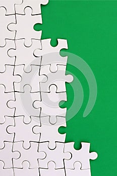 Fragment of a folded white jigsaw puzzle on the background of a green plastic surface. Texture photo with copy space for text