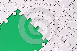 Fragment of a folded white jigsaw puzzle on the background of a green plastic surface. Texture photo with copy space for text