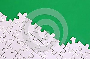 Fragment of a folded white jigsaw puzzle on the background of a green plastic surface. Texture photo with copy space for text