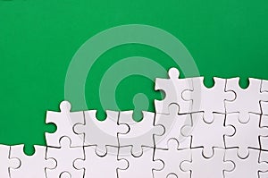 Fragment of a folded white jigsaw puzzle on the background of a green plastic surface. Texture photo with copy space for text