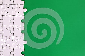 Fragment of a folded white jigsaw puzzle on the background of a green plastic surface. Texture photo with copy space for text