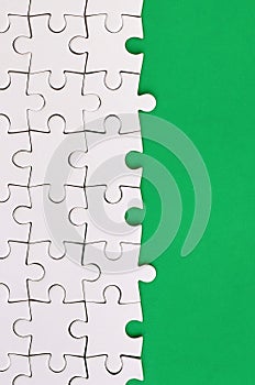 Fragment of a folded white jigsaw puzzle on the background of a green plastic surface. Texture photo with copy space for text