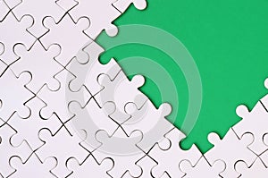 Fragment of a folded white jigsaw puzzle on the background of a green plastic surface. Texture photo with copy space for text