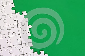 Fragment of a folded white jigsaw puzzle on the background of a green plastic surface. Texture photo with copy space for text