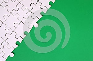 Fragment of a folded white jigsaw puzzle on the background of a green plastic surface. Texture photo with copy space for text