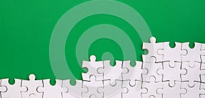 Fragment of a folded white jigsaw puzzle on the background of a green plastic surface. Texture photo with copy space for text