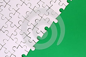 Fragment of a folded white jigsaw puzzle on the background of a green plastic surface. Texture photo with copy space for text