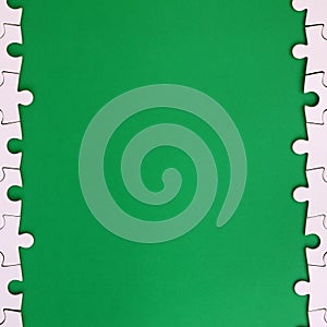 Fragment of a folded white jigsaw puzzle on the background of a green plastic surface. Texture photo with copy space for text