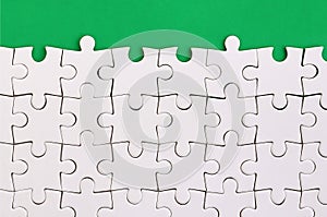 Fragment of a folded white jigsaw puzzle on the background of a green plastic surface. Texture photo with copy space for text