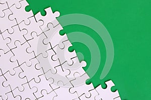 Fragment of a folded white jigsaw puzzle on the background of a green plastic surface. Texture photo with copy space for text