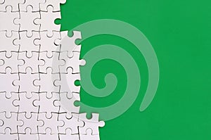 Fragment of a folded white jigsaw puzzle on the background of a green plastic surface. Texture photo with copy space for text