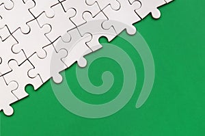 Fragment of a folded white jigsaw puzzle on the background of a green plastic surface. Texture photo with copy space for text